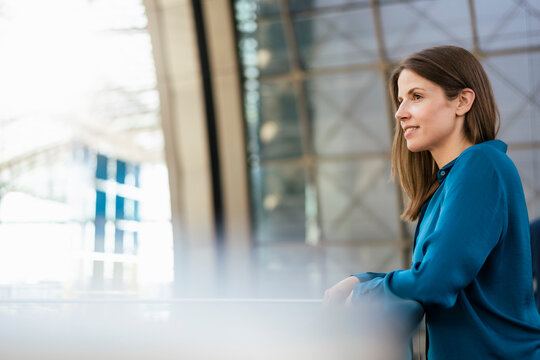 Thoughtful businesswoman leaning on railing in corridor