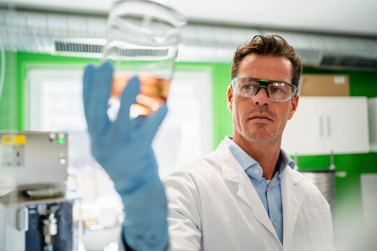Scientist wearing eyeglasses examining measuring beaker at laboratory