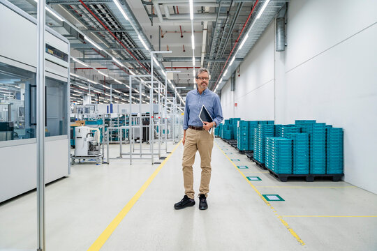 Engineer with tablet standing in production hall with machinery