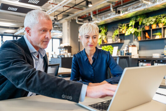 Manager and coworker point at laptop during office meeting