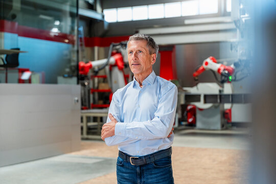 Confident manager standing in modern automated factory with robots