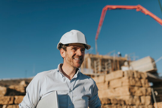Happy mature architect wearing hardhat standing at construction site