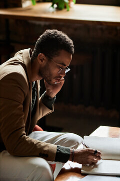 Young man talking on smart phone and writing notes in notebook
