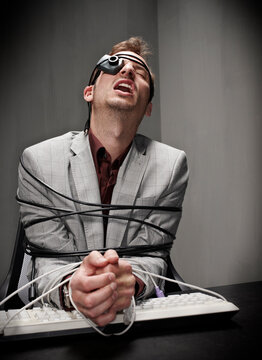 Stressed businessman tied up with computer cable at desk