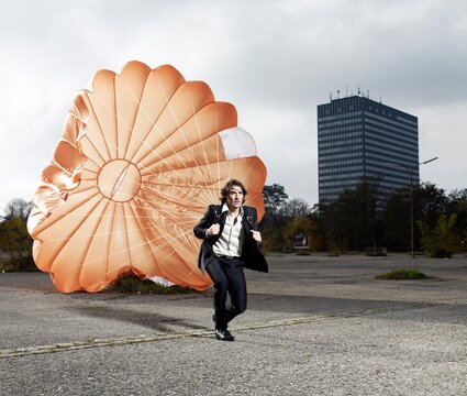 Business professional running with a parachute in the city