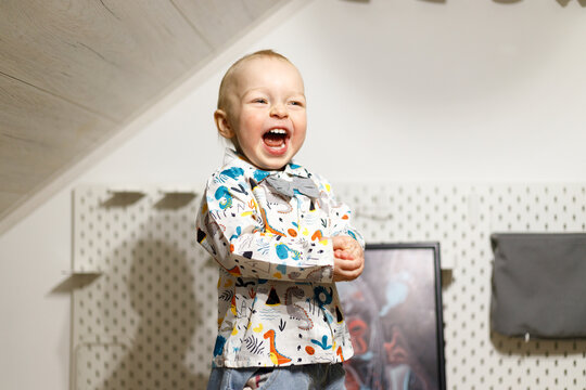 Cheerful baby boy laughing indoors wearing a patterned dinosaur shirt