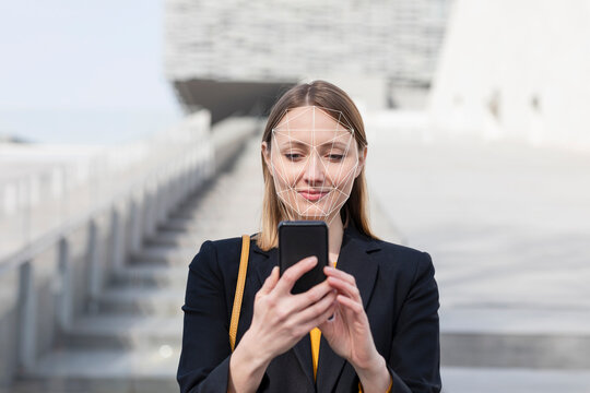 Businesswoman unlocking mobile phone with face recognition technology while standing outdoors