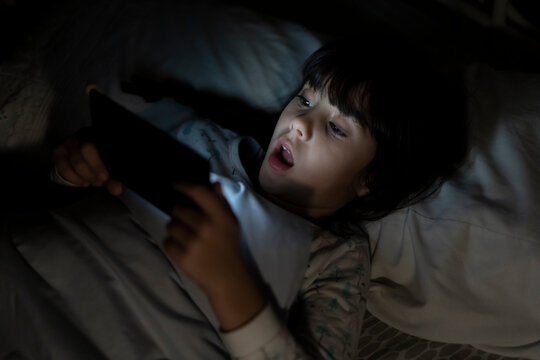 Shocked girl lying in bed using smartphone at night