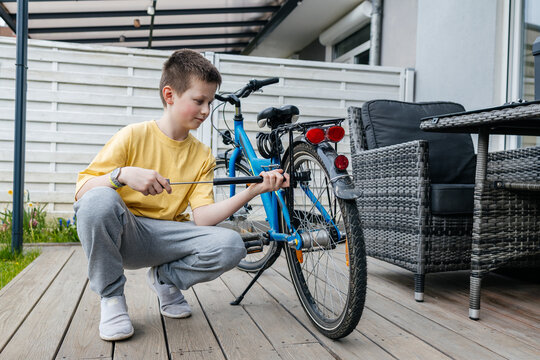 Boy inflating bicycle tire with hand pump on outdoor patio