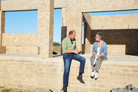 Couple sitting at building site reviewing architectural plan