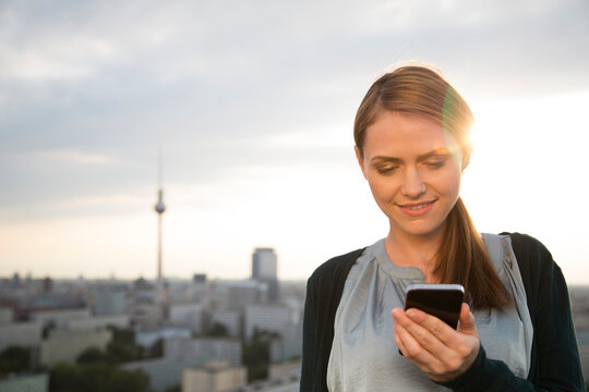 Germany, Berlin, Young woman on rooftop terrace, using mobile phone