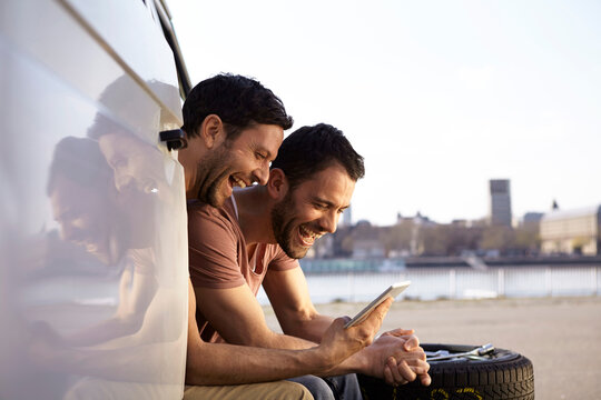 Two laughing men sitting in car looking at digital tablet