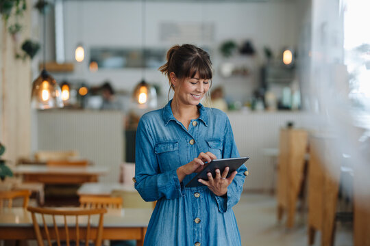 Smiling businesswoman using digital tablet while standing in coffee shop