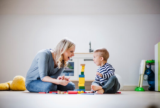 Happy mother and toddler son playing with building blocks at home