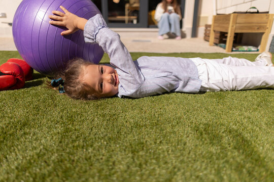 Child lying on artificial grass playing with fitness ball
