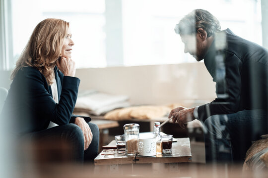 Senior female professional with hand on chin looking at male colleague discussing in cafe