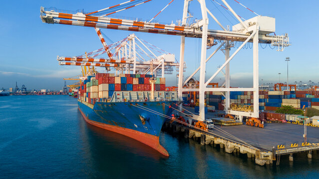 cargo container ship docked at a commercial port terminal with giant gantry cranes loading freight, representing global maritime logistics, supply chain, and international trade.