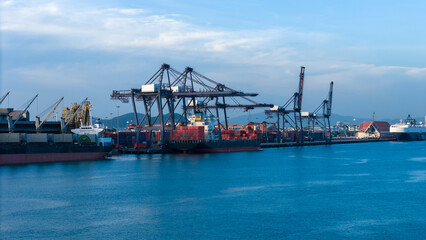Fototapeta premium cargo container ship docked at a commercial port terminal with giant gantry cranes loading freight, representing global maritime logistics, supply chain, and international trade.