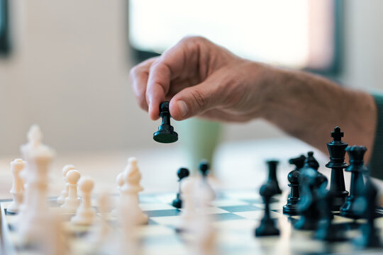 Hand moving a black pawn on a chessboard indoors