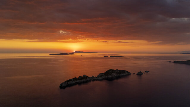 Aerial view of the islands of Mathraki and Othoni during a vibrant sunset with calm waters and a dramatic orange sky in Corfu, Greece.