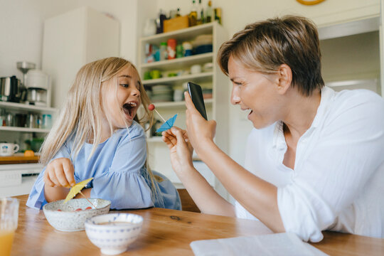 Happy mother and daughter having fun at table at home taking smartphone picture