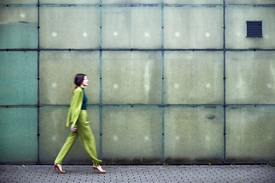 Businesswoman wearing green suit passing a wall