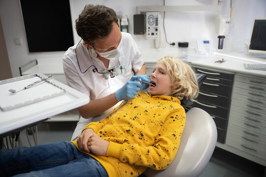 Dentist examining blond boy's teeth in medical clinic