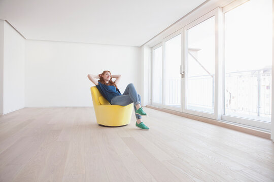Young woman sitting on yellow armchair in her empty living room