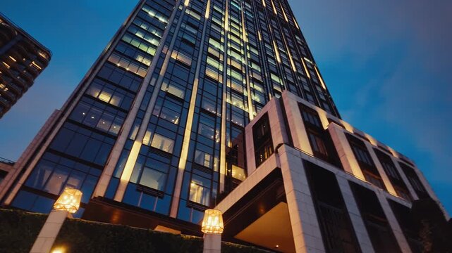 A panoramic view of a contemporary skyscraper illuminated by warm lights against a deep blue twilight sky