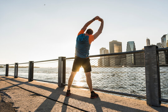 USA, Brooklyn, back view of man doing stretching exercises in the evening