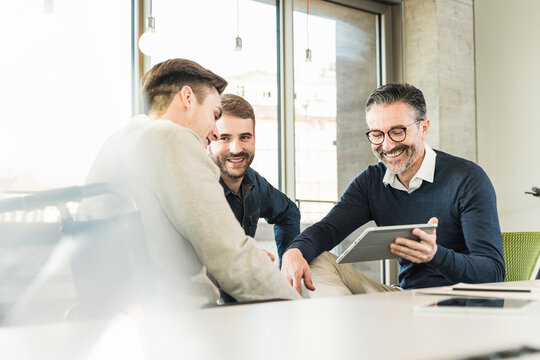 Three happy businessmen having a meeting in office sharing a tablet