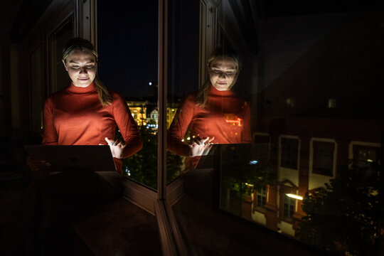 Professional woman working on tablet by window in office at night