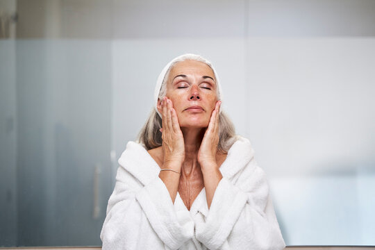 Woman with eyes closed touching face in bathroom