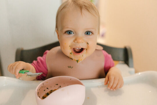 Smiling and looking at camera while eating messy food in high chair