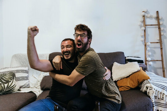 Excited male spectators screaming while watching sports in living room