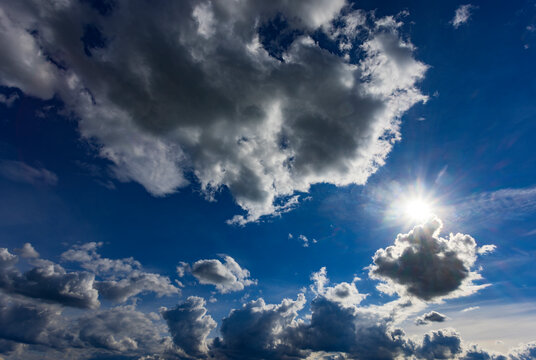 Bright sun shining through dramatic cumulus clouds in blue sky