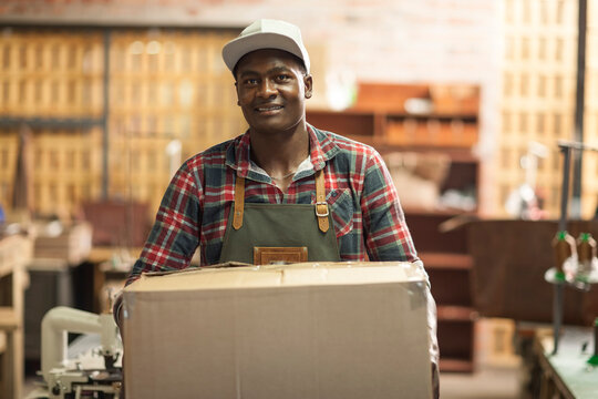 Portrait of smiling man carrying cardboard box in workshop