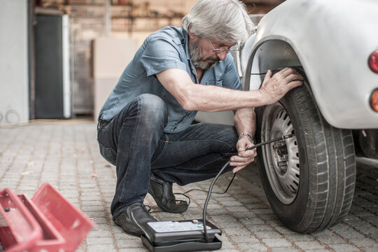 Senior man at car measuring tire pressure