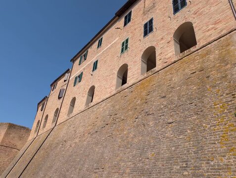 Edificio storico in mattoni a Morro d&rsquo;Alba, con archi al piano inferiore , poggiato su una parete in pietra inclinata. Cielo azzurro e atmosfera tipica dei borghi marchigiani
