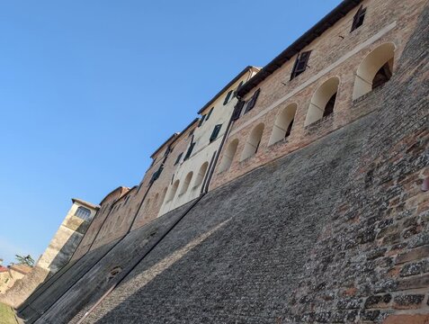 Edificio storico in mattoni a Morro d&rsquo;Alba, con archi al piano inferiore , poggiato su una parete in pietra inclinata. Cielo azzurro e atmosfera tipica dei borghi marchigiani
