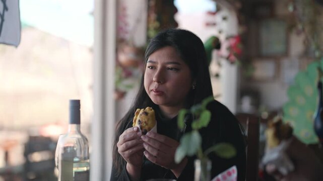 Woman in black taking a bite of a freshly baked traditional empanada at rustic, shallow depth of field restaurant setting. Static detailed view.