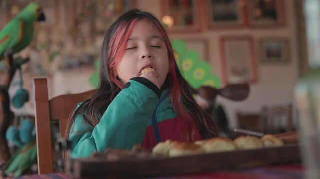 Young girl with dyed red hair at rustic restaurant, happily savoring a traditional, warm Argentine empanada. Slow motion closeup clip.