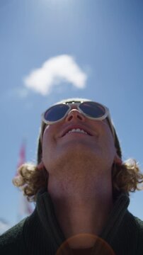 Close-up portrait of a smiling young man with Cabane Mont Fort reflected in mirrored sunglasses in Verbier, Switzerland. Unique alpine travel detail at one of the Swiss Alps&rsquo; most iconic mountain dest