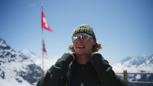 Young man wearing sunglasses and winter clothing enjoying panoramic views over the Swiss Alps in Verbier, Switzerland. Relaxed alpine lifestyle at a premium mountain destination on a sunny spring day.