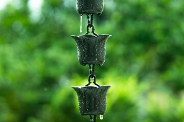 Raindrops cascading from decorative metal fixtures surrounded by lush greenery create a tranquil atmosphere, highlighting the beauty of nature and the soothing sound of rain © Kakabe