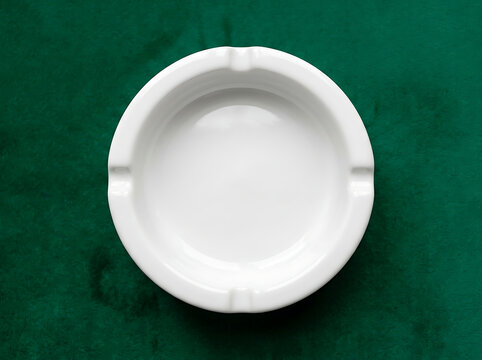 Top view of a clean white ceramic ashtray on a dark green velvet texture surface for smoking accessories and home living