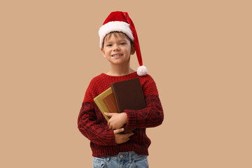 Obraz premium Cute little boy in Santa hat with books on beige background