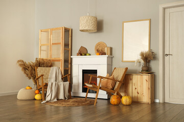 Fototapeta premium Interior of living room with armchairs, closet, dry flowers and autumn decorations on fireplace