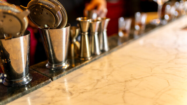 Professional bartending tools and cocktail strainers arranged on a marble bar counter in an elegant nightlife venue with copy space
