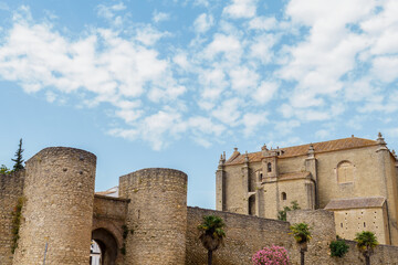 Naklejka premium Historic almocabar gate with defensive towers and the iglesia del espiritu santo under a cloudy blue sky in ronda